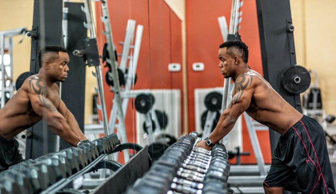 Muscular man exercising with dumbbells in gym, emphasizing strength and fitness.