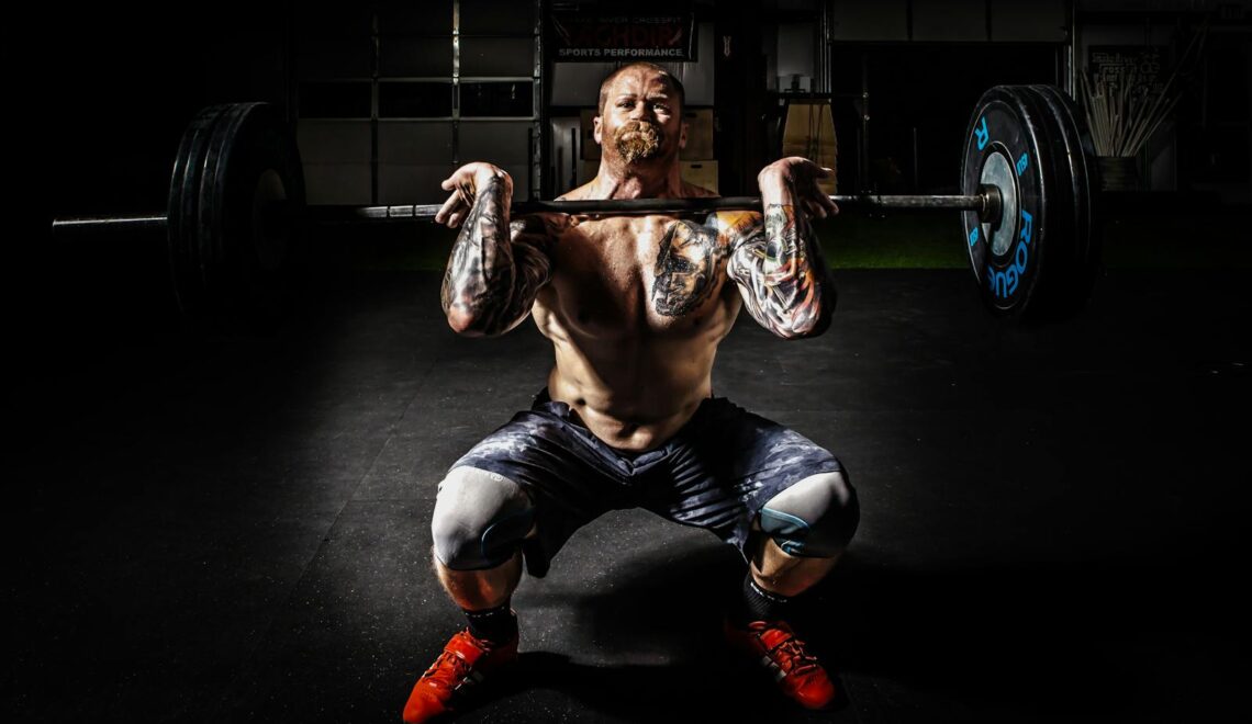 A tattooed man performing a heavy barbell squat in a gym for strength training.