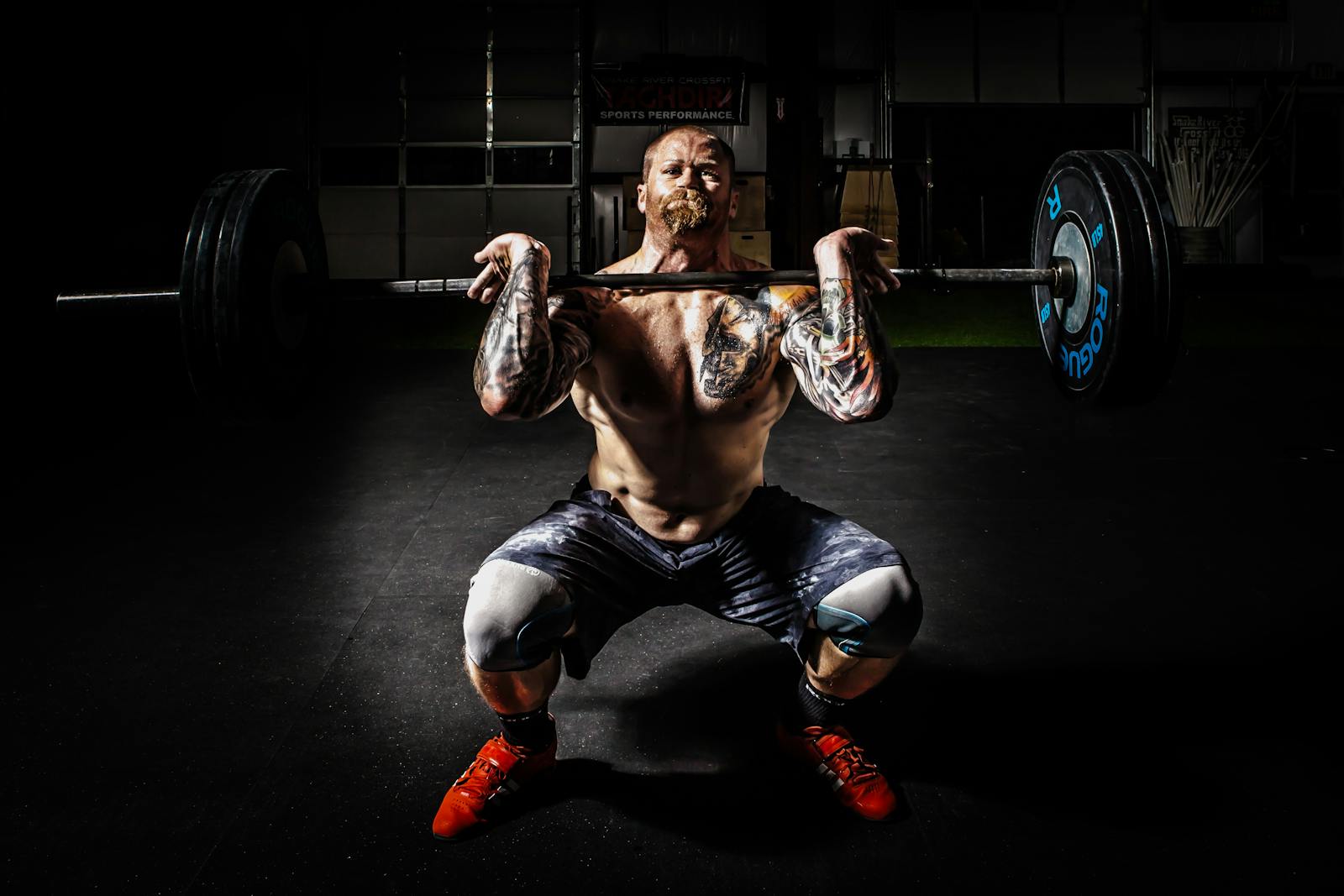 A tattooed man performing a heavy barbell squat in a gym for strength training.