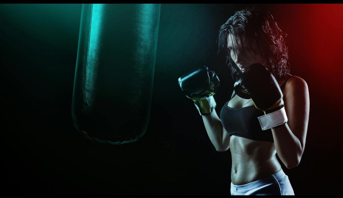 Powerful image of a woman boxer preparing to train with a punching bag in a dramatic dark setting.