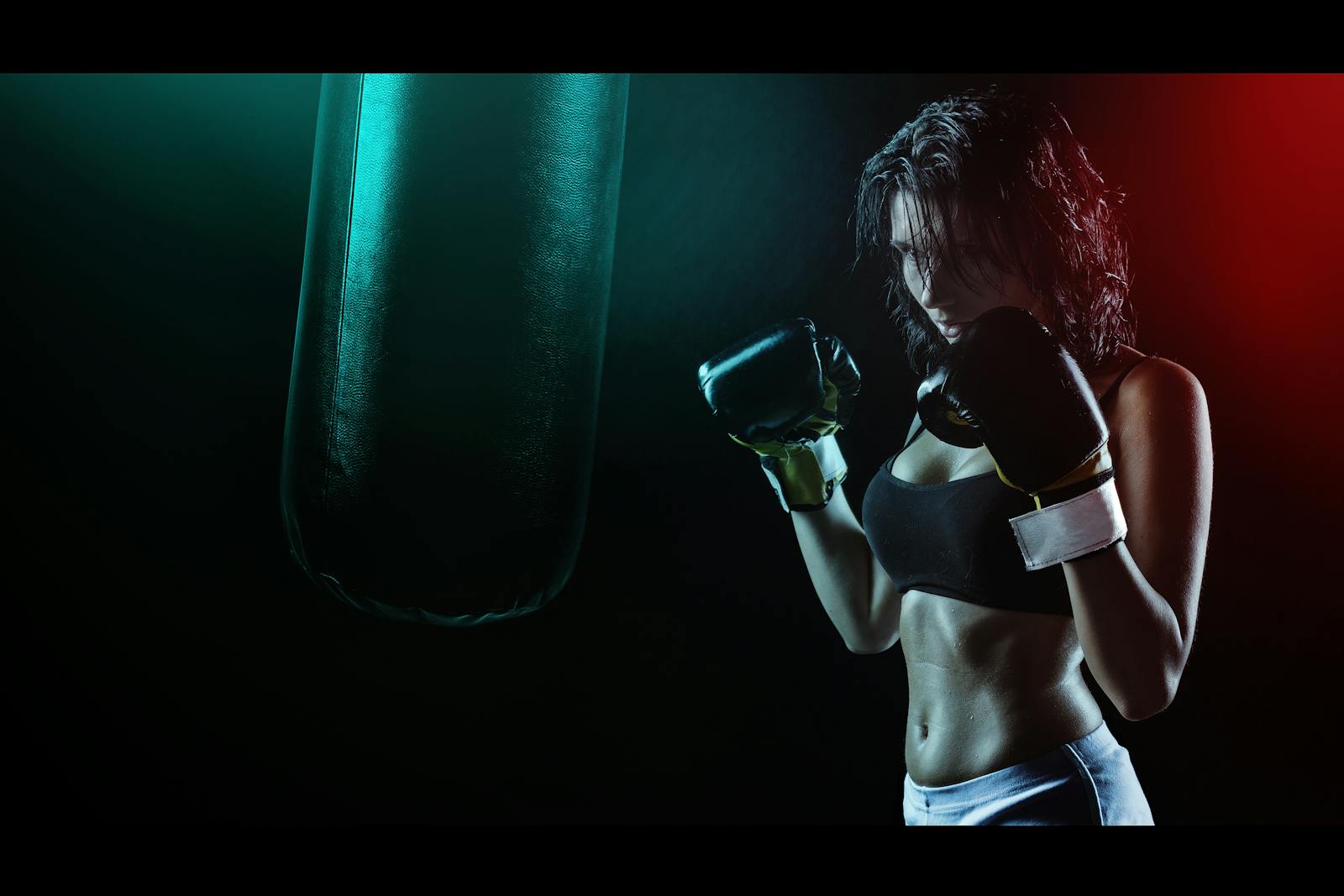 Powerful image of a woman boxer preparing to train with a punching bag in a dramatic dark setting.