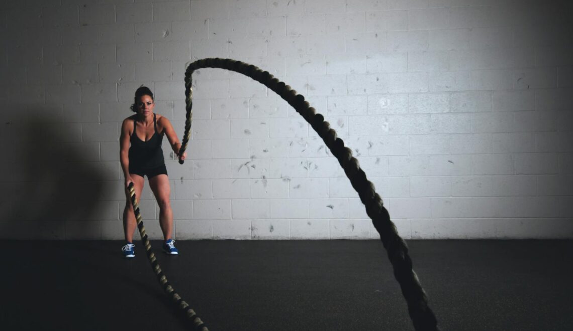 A focused woman performs a dynamic battle rope exercise in a gym setting, demonstrating strength and fitness.