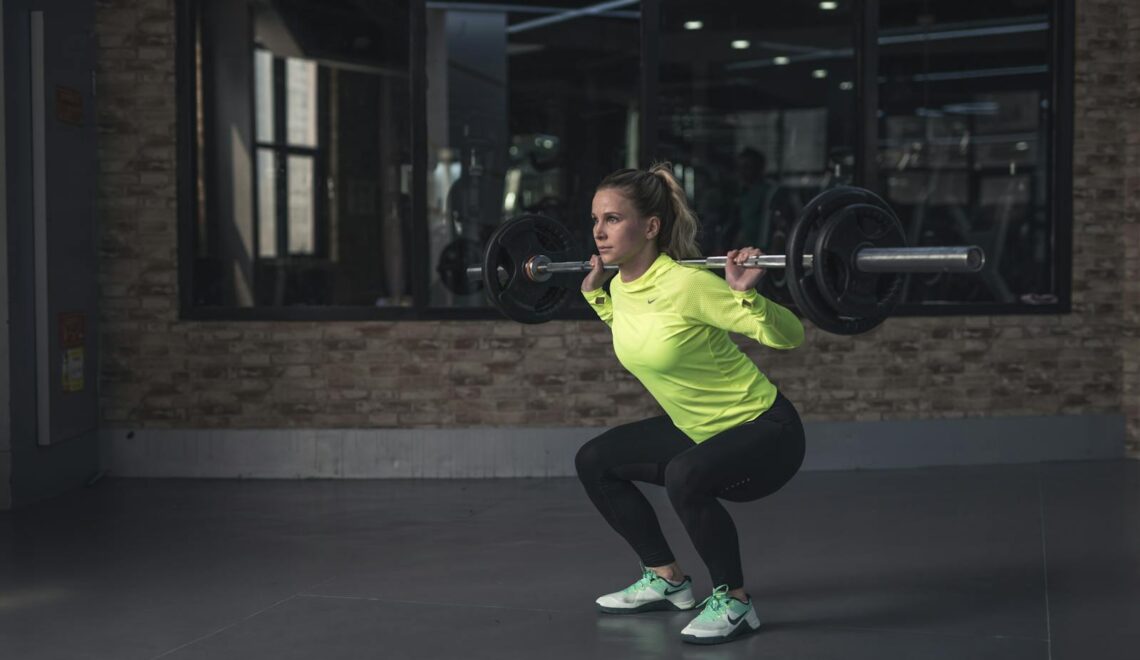 Dedicated woman in neon activewear performs a weighted squat in an indoor gym setting.