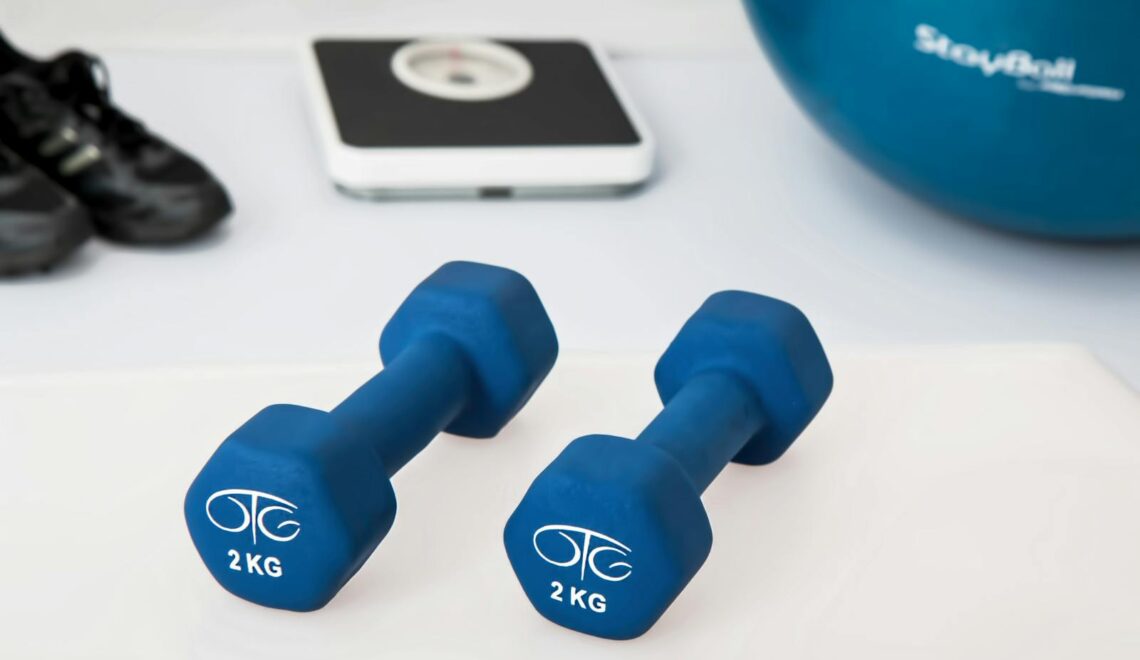 Blue dumbbells placed on a white surface with fitness equipment in the background.