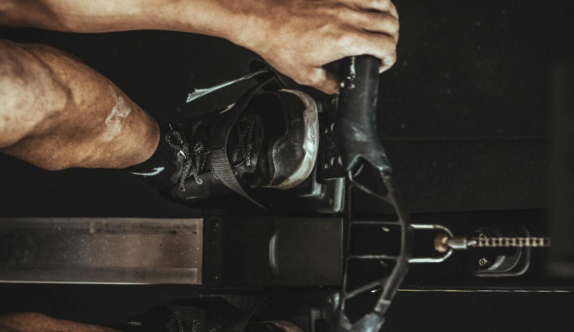 A close-up shot of a man using a rowing machine indoors, focusing on footwear and equipment.