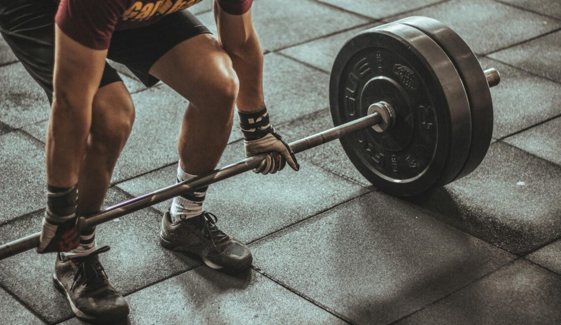 A focused weightlifter prepares to lift a heavy barbell in an indoor gym setting.